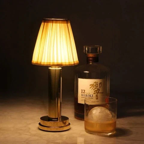 Cordless brass table lamp with fabric shade on a wooden table, portable for home decor