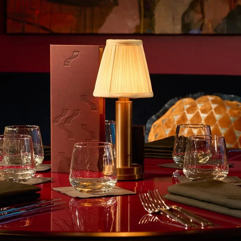 Cordless brass table lamp with fabric shade on a wooden table, portable for home decor