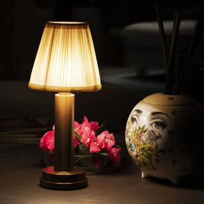 Cordless brass table lamp with fabric shade on a wooden table, portable for home decor