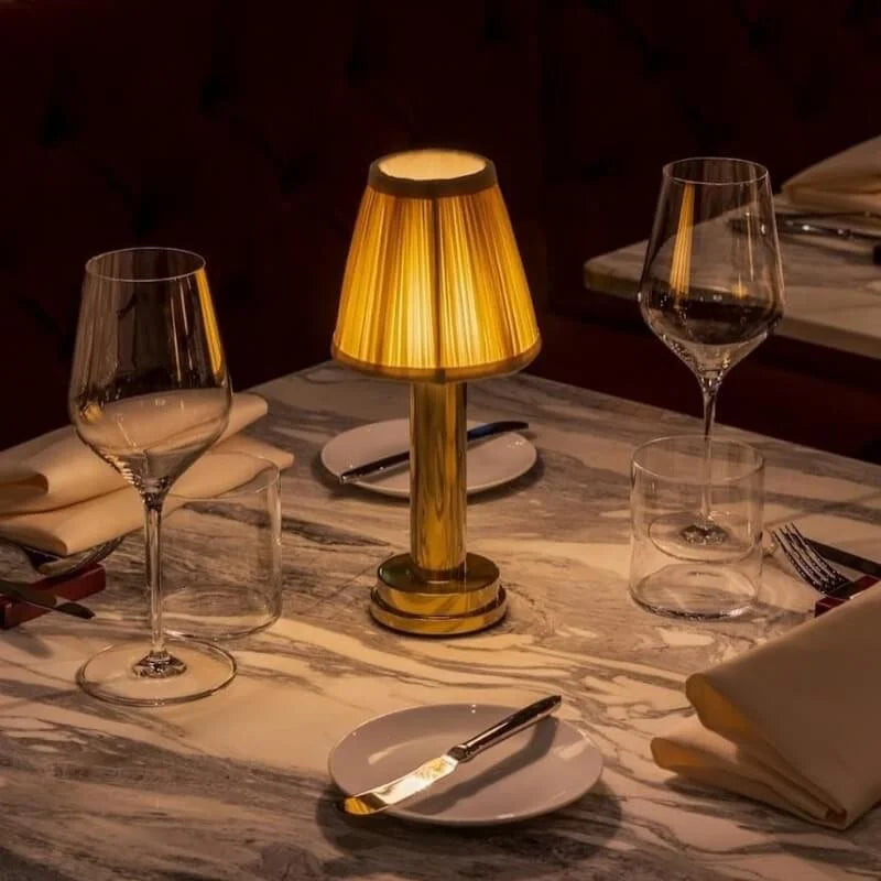 Cordless brass table lamp with fabric shade on a wooden table, portable for home decor