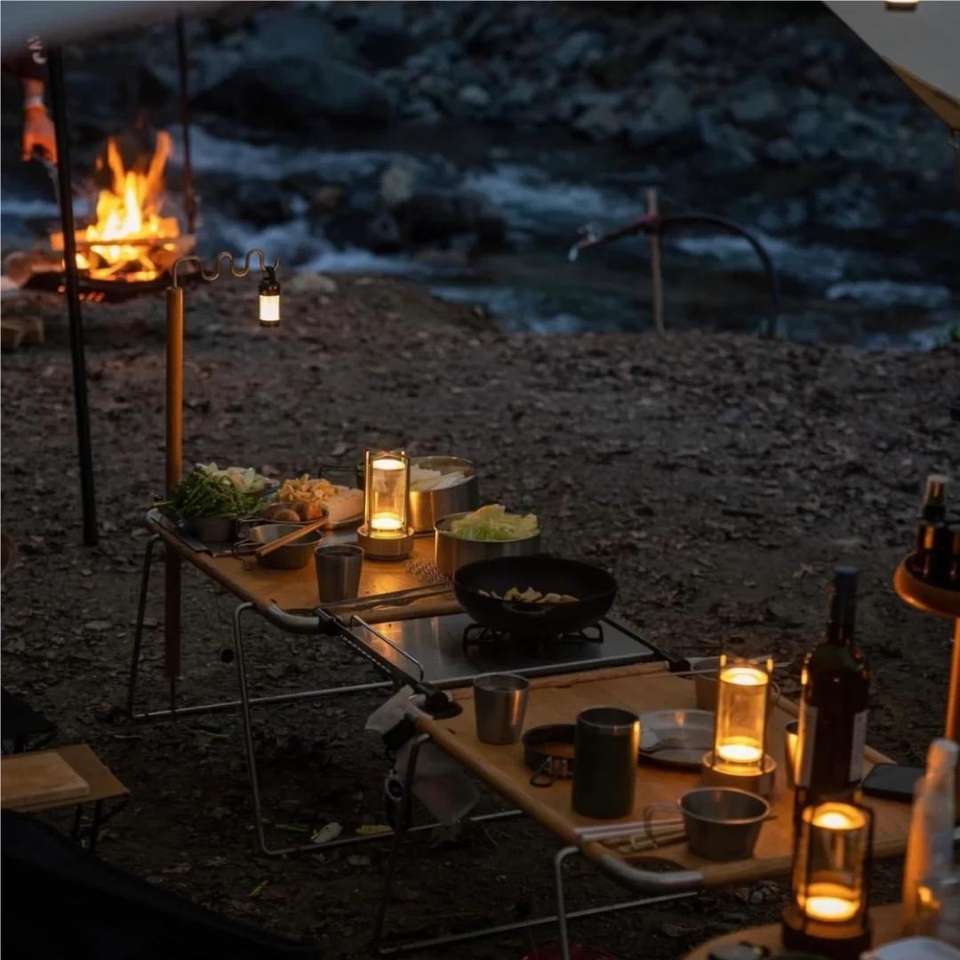 Cordless table lamp with metal cage and warm glow on a camping table