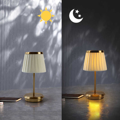 Cordless rechargeable table lamp with gold frame and fabric shade on a desk