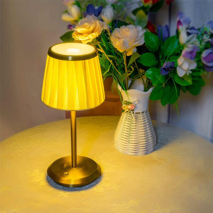 Cordless rechargeable table lamp with gold frame and fabric shade on a desk