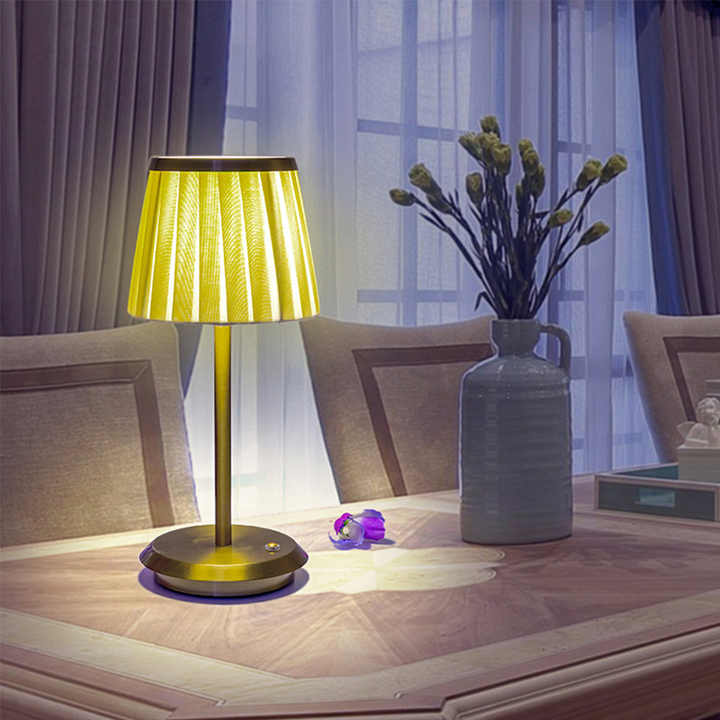 Cordless rechargeable table lamp with gold frame and fabric shade on a desk