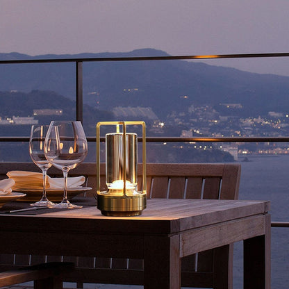 Cordless table lamp with metal cage and warm glow on a camping table