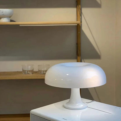 Mushroom-shaped acrylic table lamp with a warm glow on a bedside table
