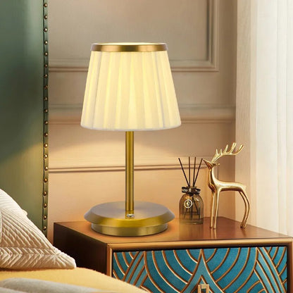 Cordless rechargeable table lamp with gold frame and fabric shade on a desk