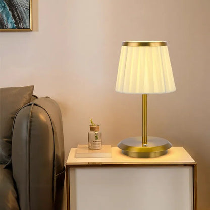 Cordless rechargeable table lamp with gold frame and fabric shade on a desk