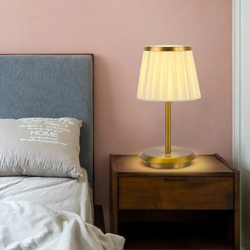 Cordless rechargeable table lamp with gold frame and fabric shade on a desk