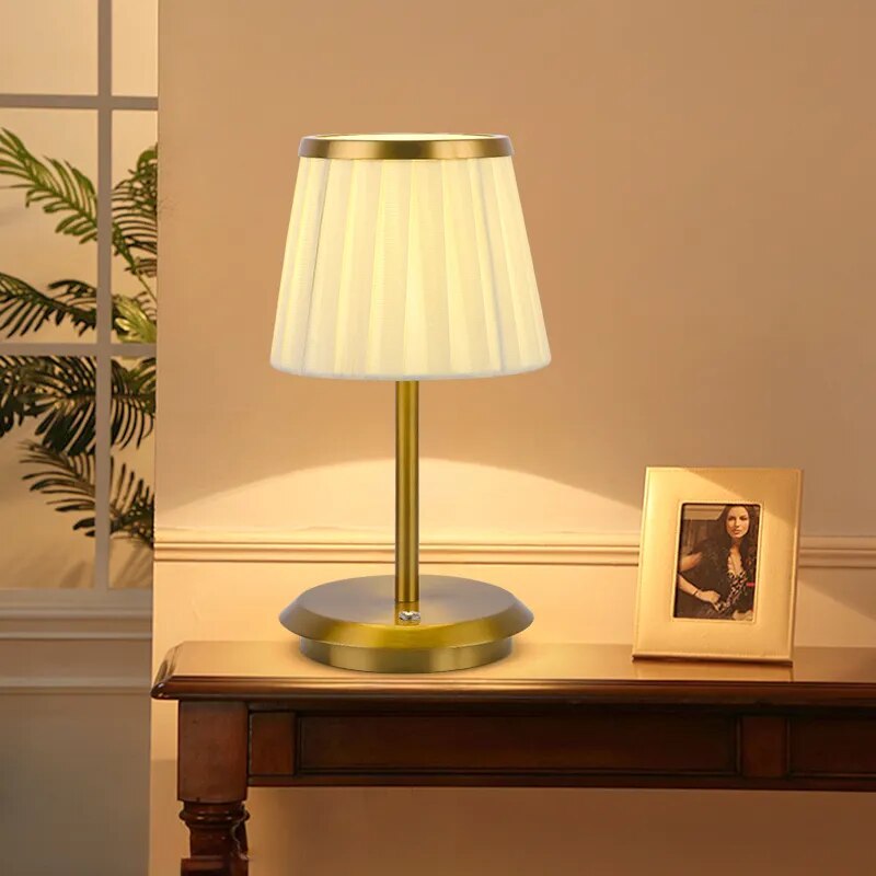 Cordless rechargeable table lamp with gold frame and fabric shade on a desk