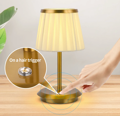Cordless rechargeable table lamp with gold frame and fabric shade on a desk