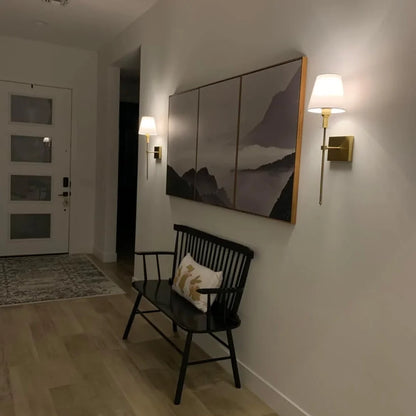 Rechargeable wireless wall sconce with metal and cloth shade, mounted on a wall in a living room, no cords visible