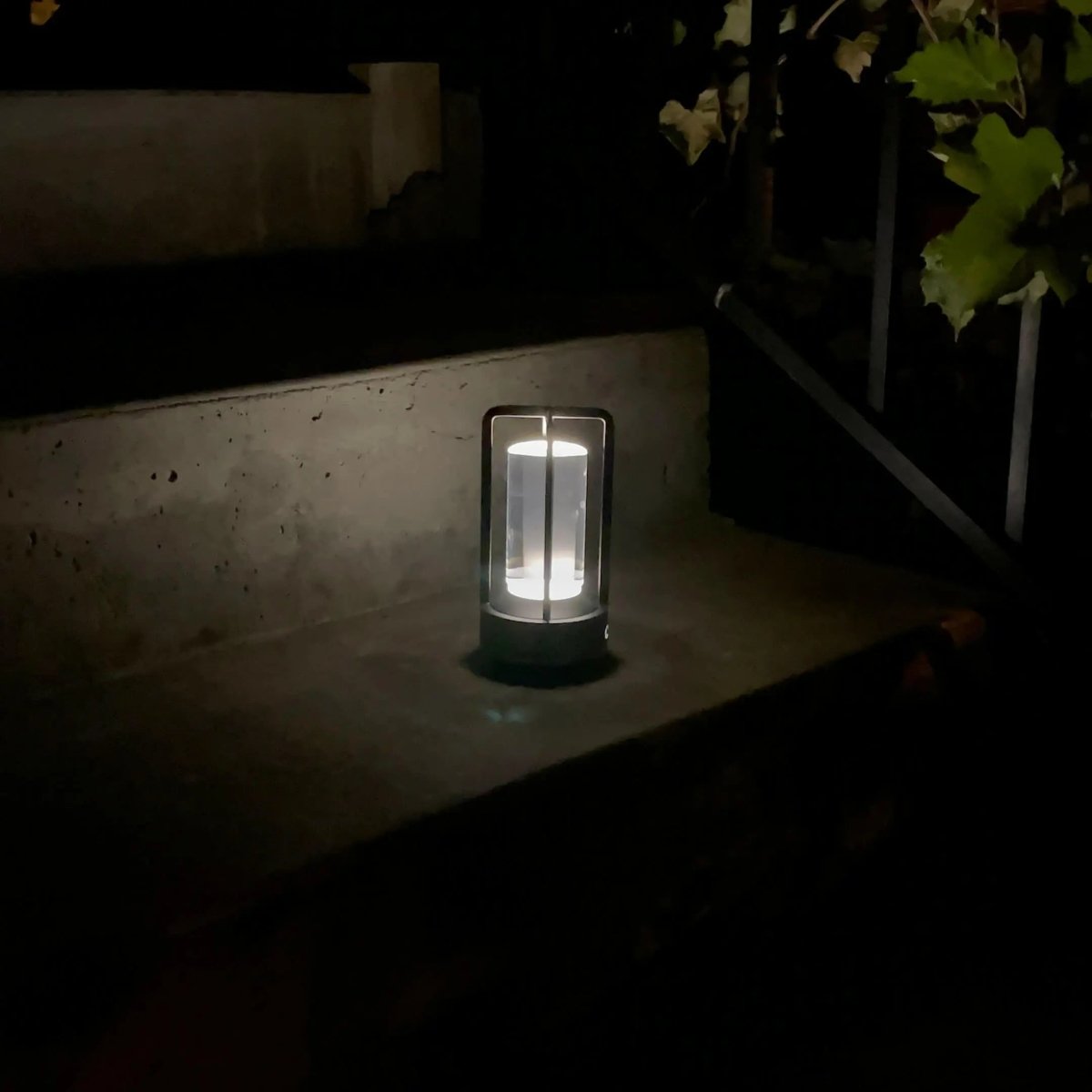 Cordless table lamp with metal cage and warm glow on a camping table