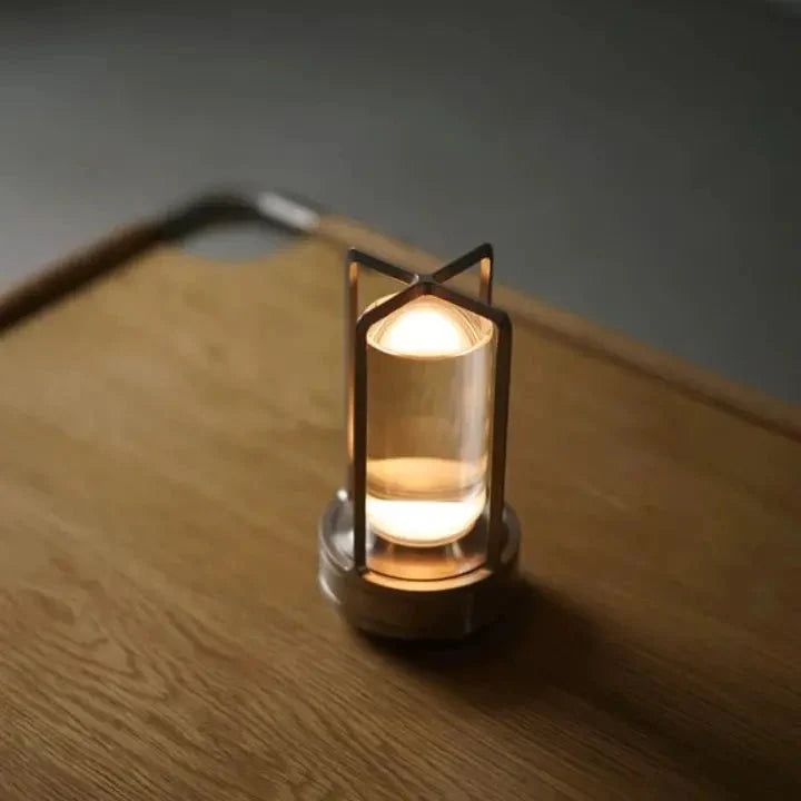 Cordless table lamp with metal cage and warm glow on a camping table